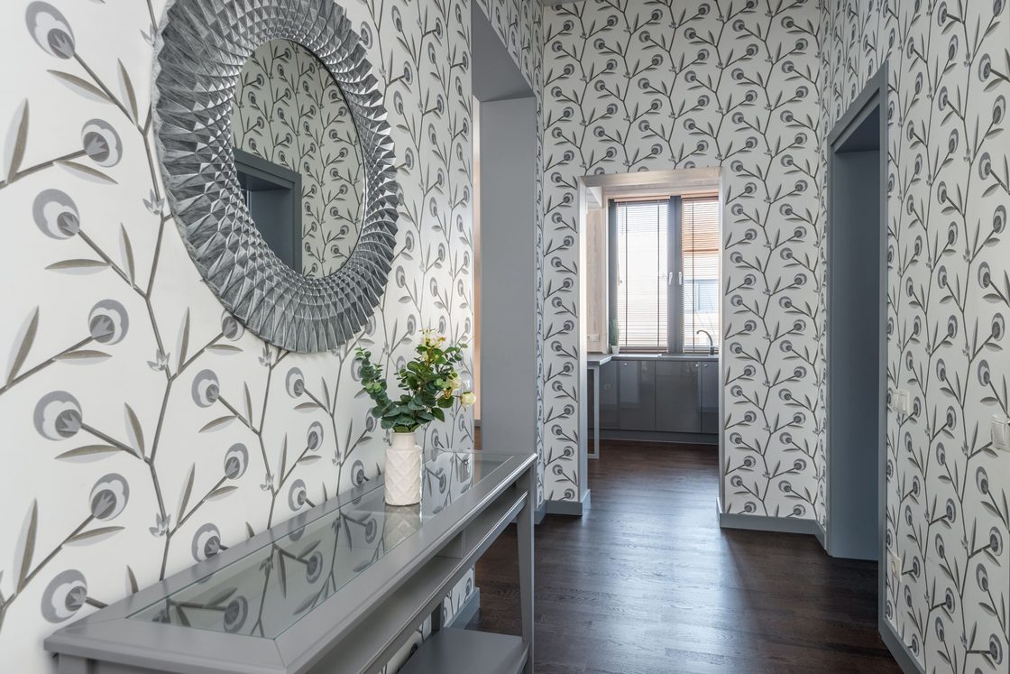 Bright hallway finished in soft grey botanical wallpaper with a round mirror and console