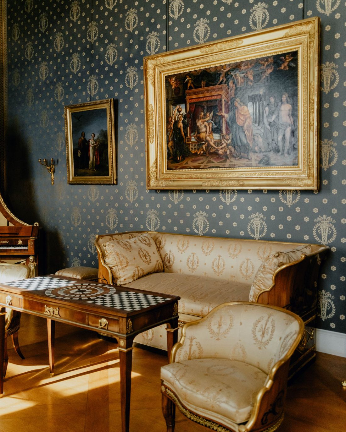 Formal sitting room with slate-blue wallpaper in a gold crest pattern and framed artwork