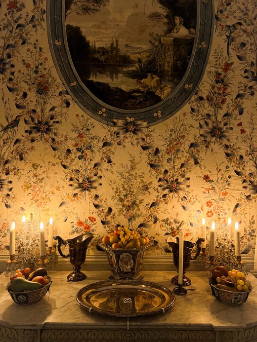 Candlelit corner with dark floral wallpaper and a framed landscape print