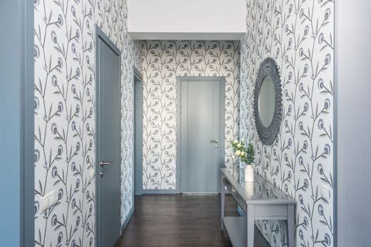 Hallway lined with soft blue paisley wallpaper and a round mirror