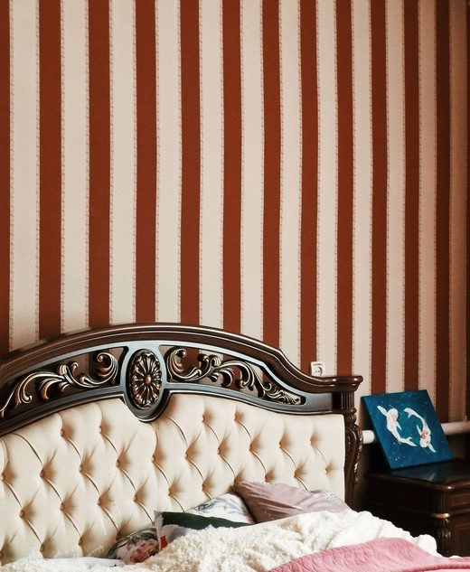 Bedroom with warm vertical-stripe wallpaper behind a carved, tufted headboard