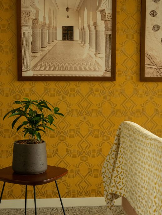 Room corner in mustard-yellow geometric trellis wallpaper with framed prints