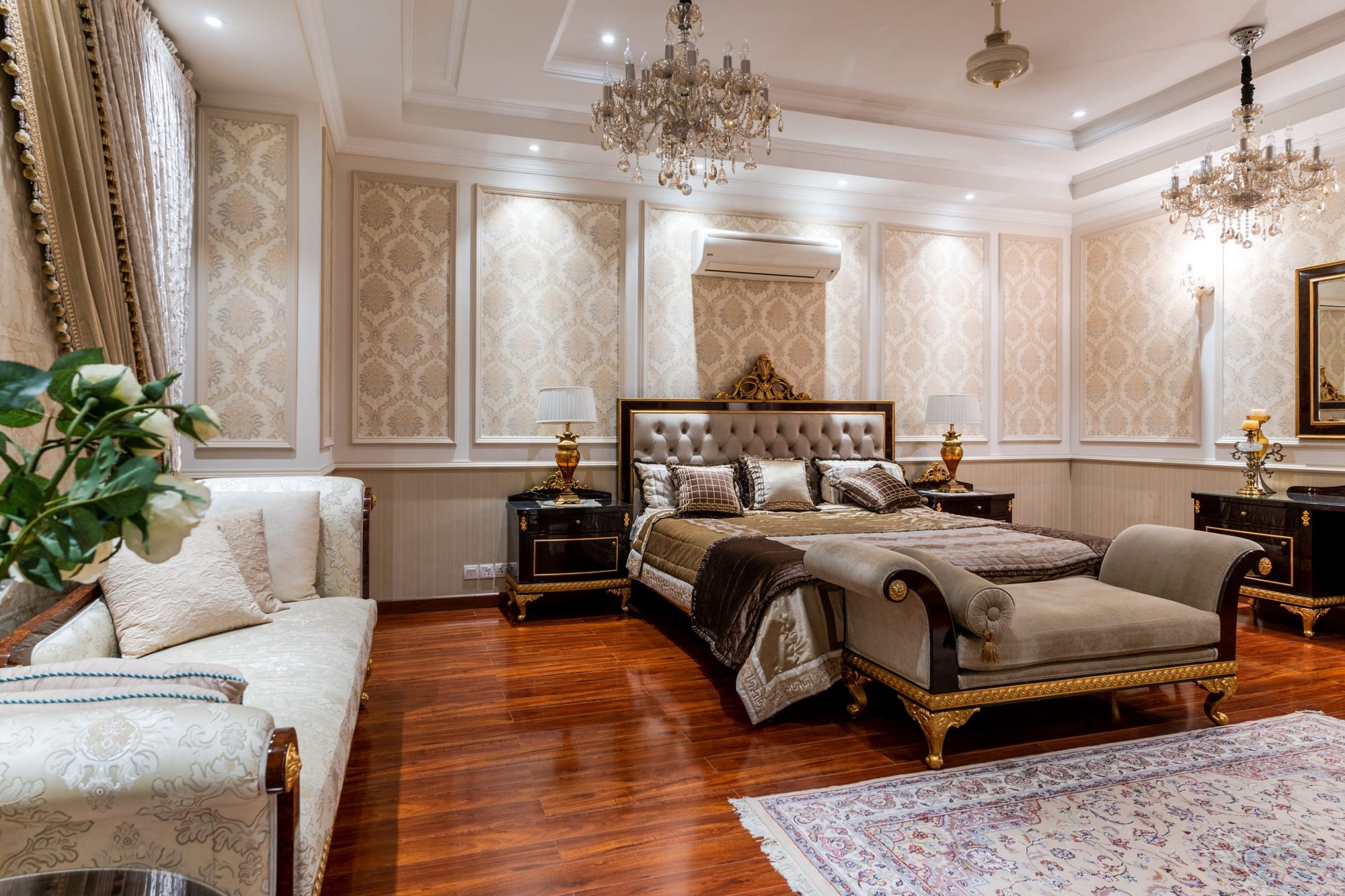 Elegant traditional bedroom with cream damask wallpaper panels, a tufted headboard and crystal chandeliers