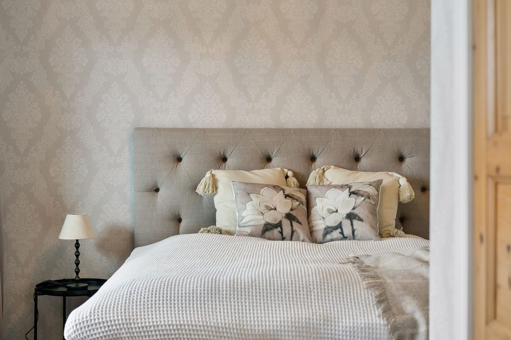 Refined bedroom with subtle tone-on-tone damask wallpaper behind an upholstered headboard